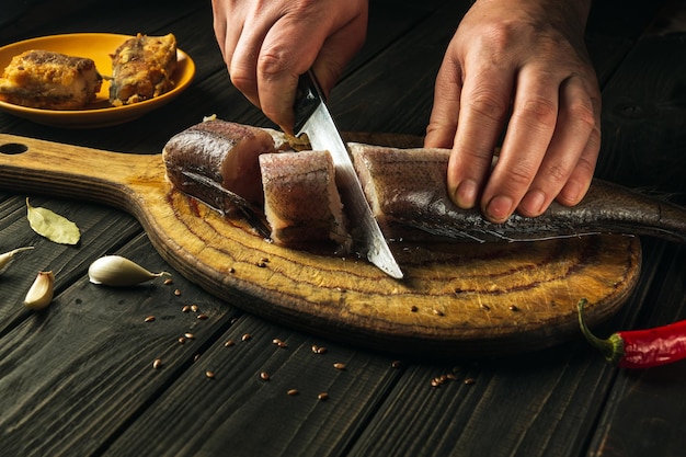 The chef cuts fresh Merluccius fish on a wooden cutting board with a knife.