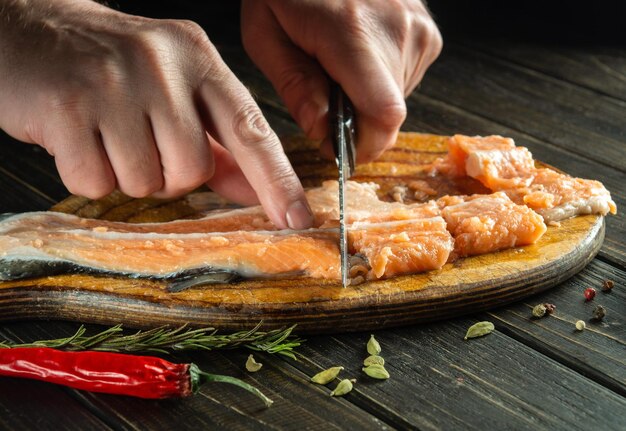 The chef cuts fresh salmon fish with a knife on a kitchen cutting board Cooking a delicious fish dish according to an old recipe with the addition of spices and pepper