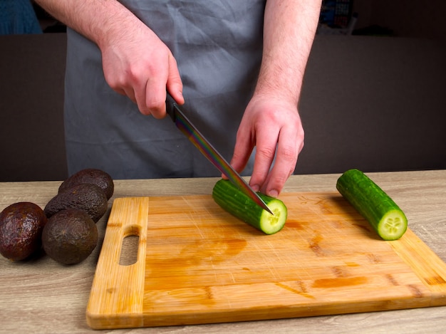 Chef cuts a green cucumber with a knife on a wooden board