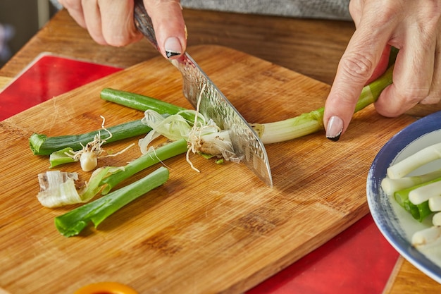 Chef cuts the leek in circles in the kitchen on wooden board