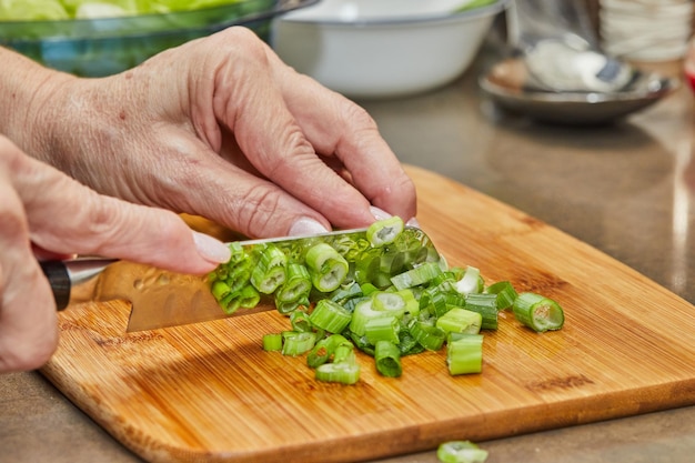 Chef cuts leek on wooden board in the kitchen