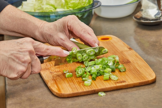 Chef cuts leek on wooden board in the kitchen