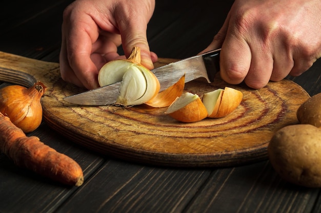 The chef cuts the onion with a knife on a wooden chopping board