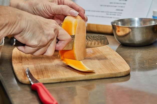 Chef cuts pumpkin in the shape of pear on wooden board in the home kitchen