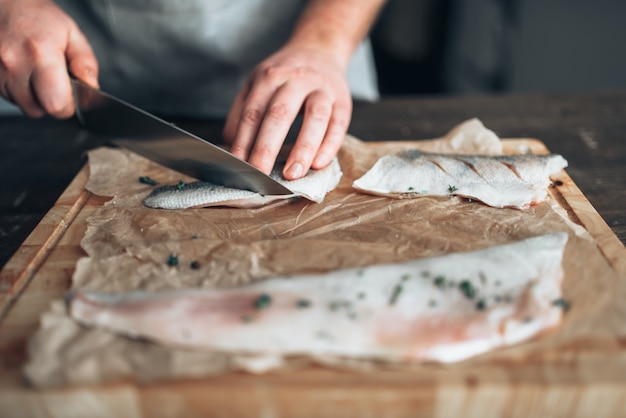 Photo chef cuts raw fish slices on wooden cutting board