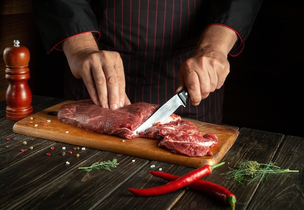 The chef cuts raw fresh beef meat on a cutting board before baking or grilling Working environment in the kitchen of a restaurant or hotel