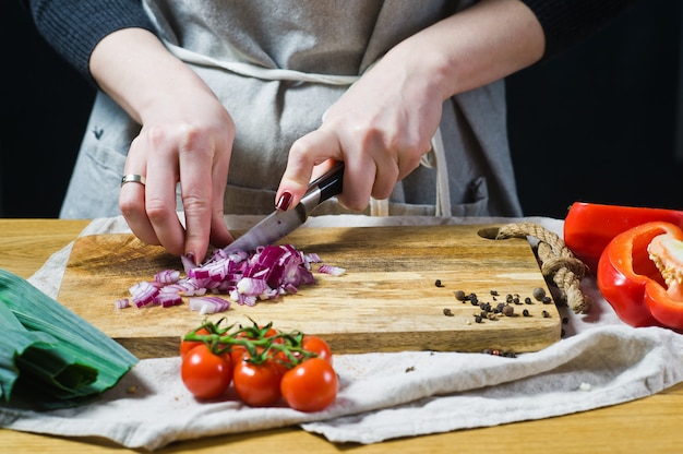 The chef cuts red onions on a wooden chopping Board. 