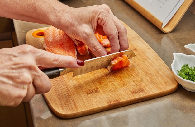 Chef cuts the salmon into cubes with knife to prepare the dish according to the recipe