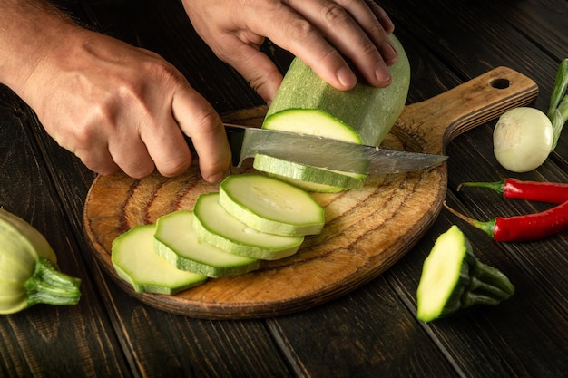 The chef cuts vegetable marrow into small pieces with a knife before fire or cooking delicious food