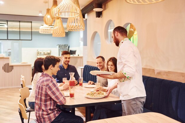 Chef delivers food Group of young friends that sitting together indoors and eating pizza