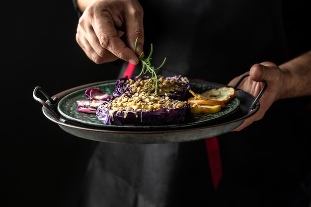 Chef finishing her plate Only hands Finally dish dressing red cabbage baked with nuts quince and apples adds a sprig of fresh rosemary