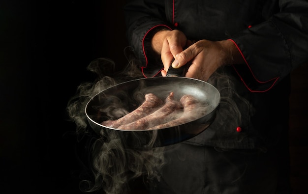 Chef fry sausages on a hot pan with steam Menu or recipe concept for hotel on black background