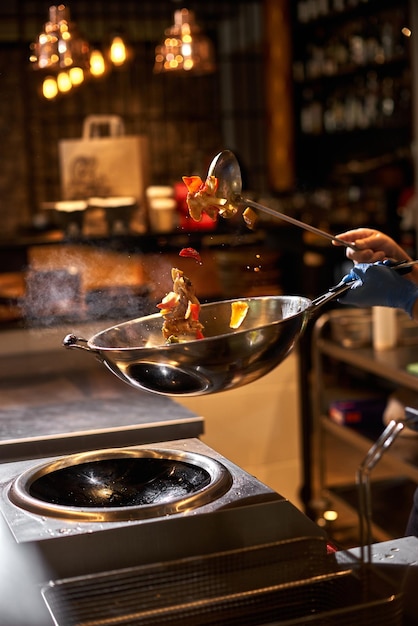 Chef hand keep wok Closeup hands tossing food at professional dark kitchen Chef in prepare asian food