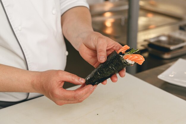 Chef hands cooking sushi with rice salmon and nori on kitchen of japanese restaurant