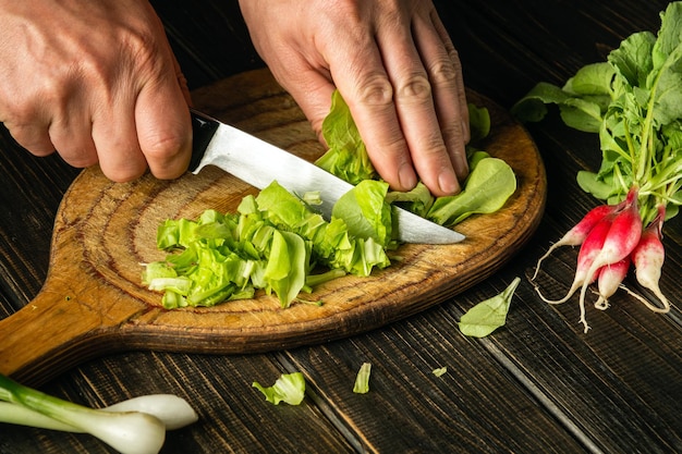 Chef hands cutting green lettuce leaves on a cutting board with a knife for preparing a vegetarian