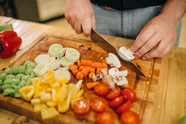 Photo chef hands with knife cuts mushrooms on wooden board closeup