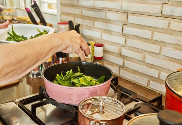 Chef is frying sorrel in frying pan in oil on gas stove