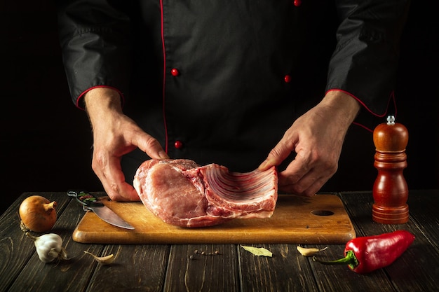 The chef is holding a piece of raw meat with a bone in the kitchen