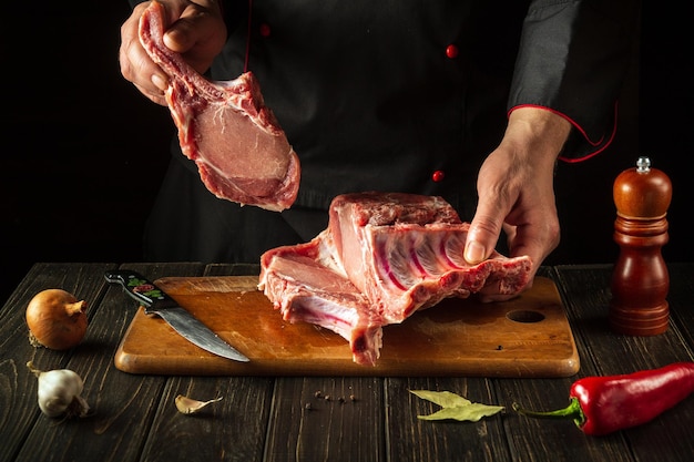 The chef is holding a piece of raw meat with a bone in the kitchen