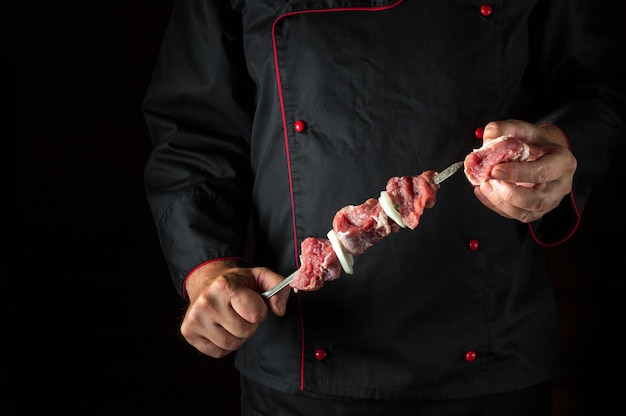 Photo the chef is holding a shish kebab with raw lamb meat and onions on a skewer