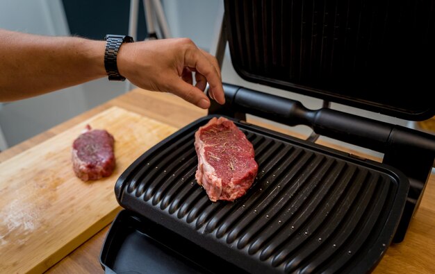 Chef at the kitchen preparing beef steaks on the home electric grill