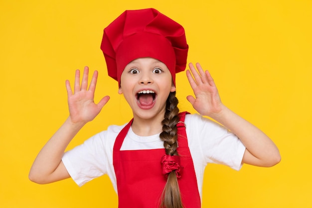 Chef little girl is going to cook dishesThe profession of a cook for children Cooking for children A child in a red apron and a cap on a yellow isolated background