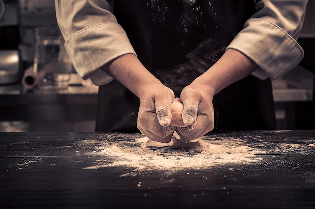 The chef makes dough for pasta on a wooden table