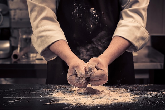 The chef makes dough for pasta on a wooden table