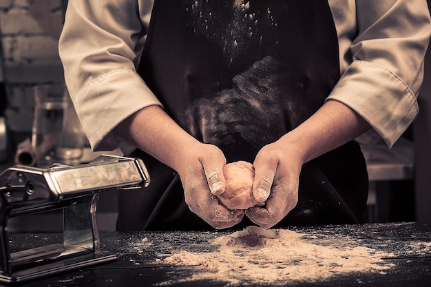 The chef makes dough for pasta on a wooden table