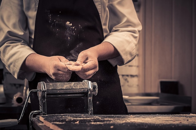 The chef makes dough for pasta on a wooden table