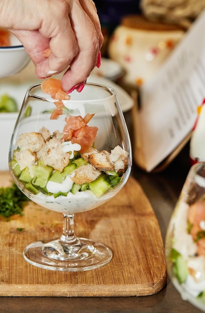 Chef makes Summer salad in glass of salmon cucumbers croutons herbs and fresh cream Elegant Summer Fusion