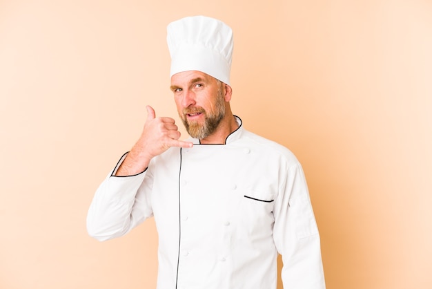 Chef man isolated on beige wall showing a mobile phone call gesture with fingers.