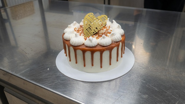 Chef pastry baker finishing salty caramel frosted dripping cakes with meringues and chocolate heart topper