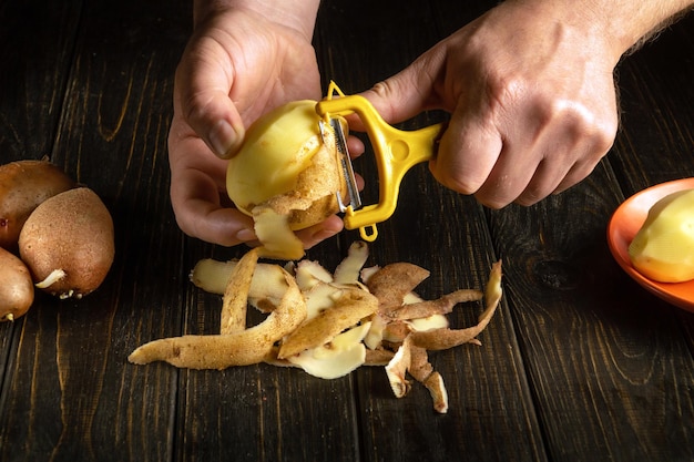 The chef peels raw potatoes in a hotel kitchen before preparing a national dish Closeup of a cook hands with a potato peeler while working