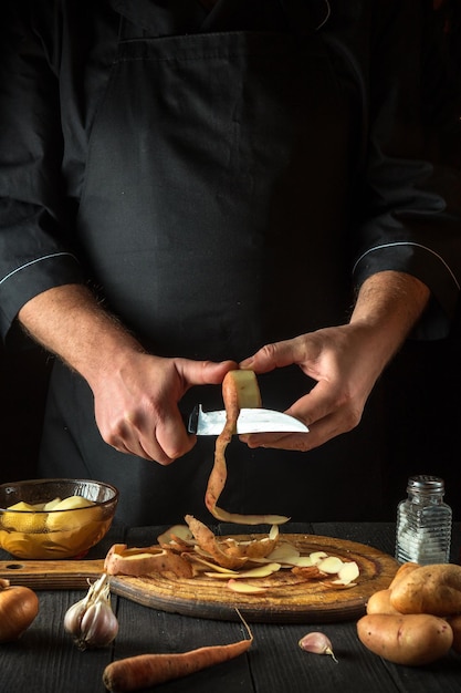 The chef peels raw potatoes in a restaurant kitchen before preparing a national dish