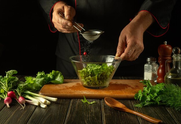 The chef peppers chopped lettuce leaves in a bowl Working environment in a restaurant kitchen Delicious salad with fresh vegetables