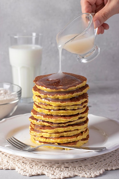 Chef pouring condensed coconut milk on coconut flour pancakes vegan food gray background