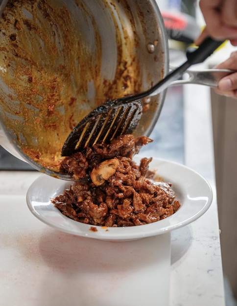 Chef pouring fried beef with mushroom from a pan on white dish