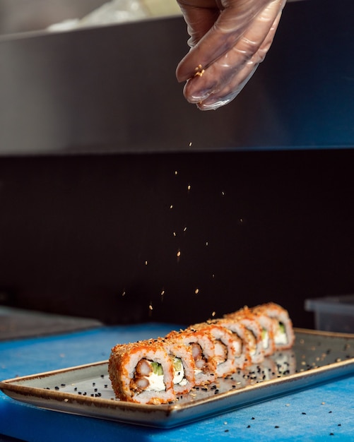 Chef pouring sesame seeds to the Kani sushi hot roll close up