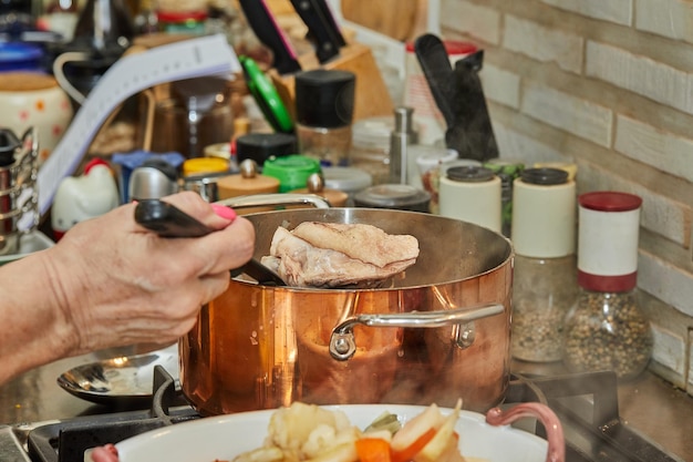 Chef pours chicken broth from copper pot into dish of chicken legs