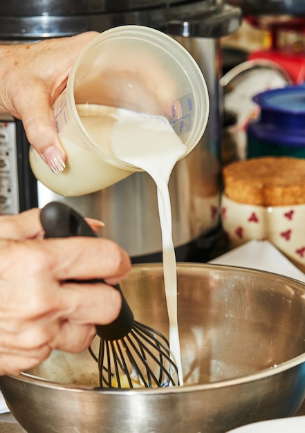 Chef pours milk from measuring glass into bowl and stirring it with whisk.