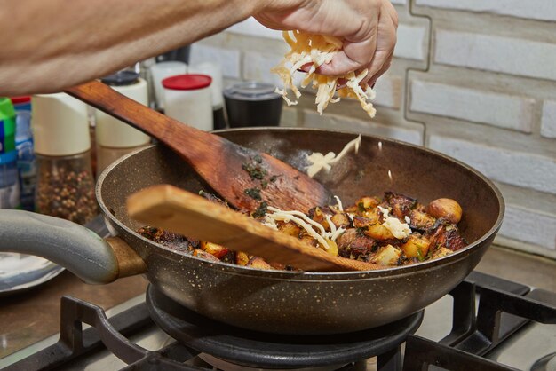 Chef pours parmesan into a frying pan with fried potatoes chestnuts parsley and wooden spatulas on gas stove Step by step recipe