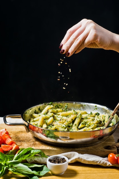 Photo chef pours sauce into penne pasta with spinach. 