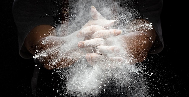 Photo chef prepare white flour dust for cooking bakery food elderly man chef clap hand white flour dust explode fly in air flour stop motion in air with freeze high speed shutter black background