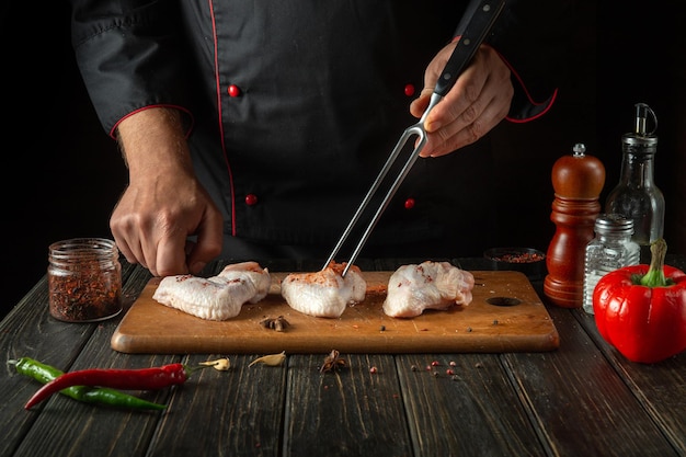 The chef prepares raw chicken wings with spices and peppers in the kitchen Asian cuisine Space for advertising on a dark background