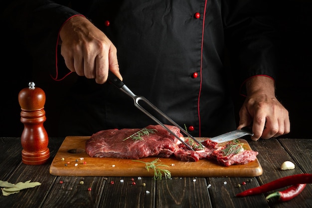 The chef prepares raw meat on a kitchen cutting board Idea for a hotel menu on a dark background