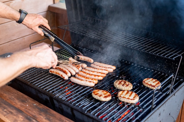 Chef preparing meat on the grill during outdoor outside food festival food truck brunch or catering event pork steaksbavarian sausagesbarbecue party summer barbecue party or picnic in backyard