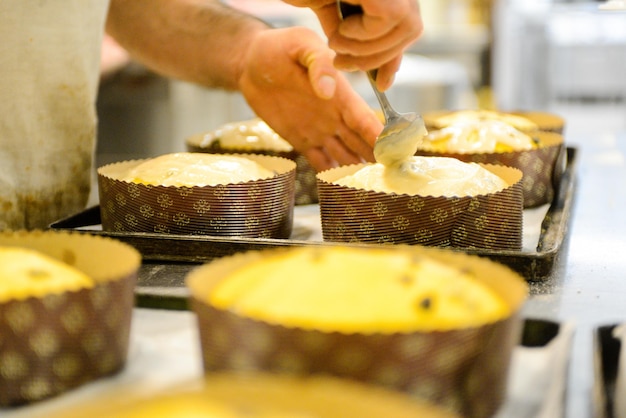 Chef producing panettone while lievitate adding almond sugar topping to raw sweet bread