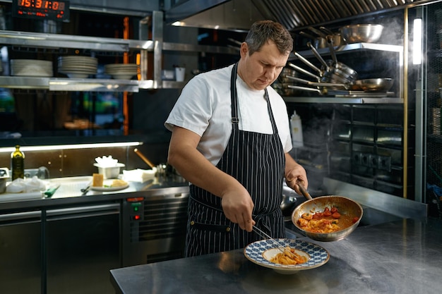 Chef putting spaghetti carbonara on plate standing on restaurant kitchen