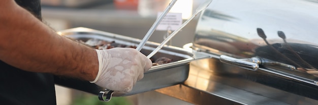 Chef in rubber gloves holding metal tray with food and tongs closeup